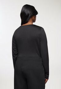 Czarny top z długim rękawem wykonany z gładkiego materiału, z okrągłym dekoltem. W zestawie z pasującymi czarnymi spodniami o wysokim stanie.