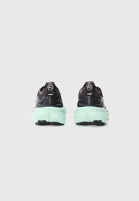 Une paire de chaussures de course Puma noires et vert menthe montrées de l'arrière sur un fond blanc uni.