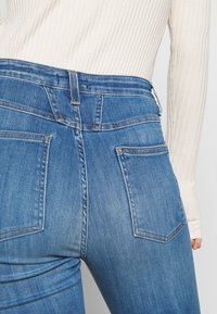 Jeans de mezclilla azul oscuro con una cintura alta, dos bolsillos traseros y detalles de costura sutiles. La tela tiene una textura suave y un ligero estiramiento.