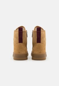 Bottines en suède beige avec des accents bordeaux profonds, fermeture à glissière sur le côté et semelle en caoutchouc texturée. Design à bout rond.