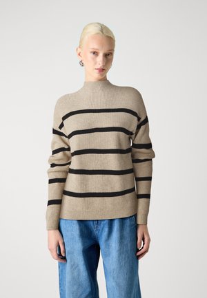 Beige ribbed sweater with black horizontal stripes, high neckline, and long sleeves, paired with loose blue jeans.