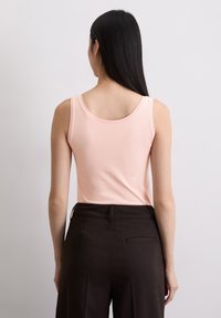 Roze tanktop van zacht materiaal met een ronde rug, gecombineerd met donkere broeken met een achterzak en een getailleerde pasvorm.