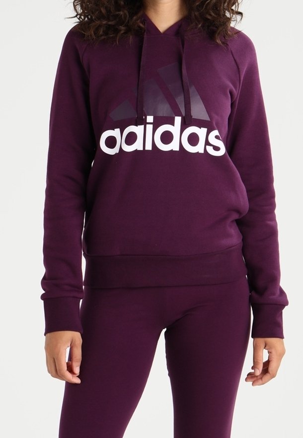 Mujer vistiendo una sudadera con capucha morada y leggings a juego, con un logo blanco y morado oscuro de "aadidas" en el frente.
