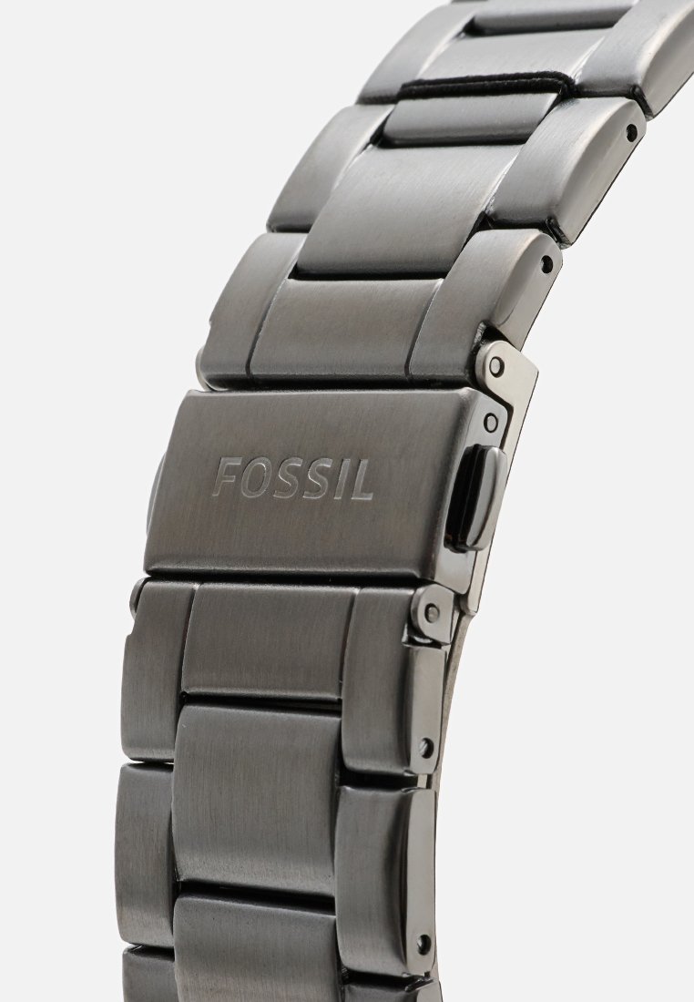 Bracciale in metallo con finitura grigio scuro spazzolato, con design a maglie, logo Fossil sulla chiusura, texture liscia e dettagli lucidi.