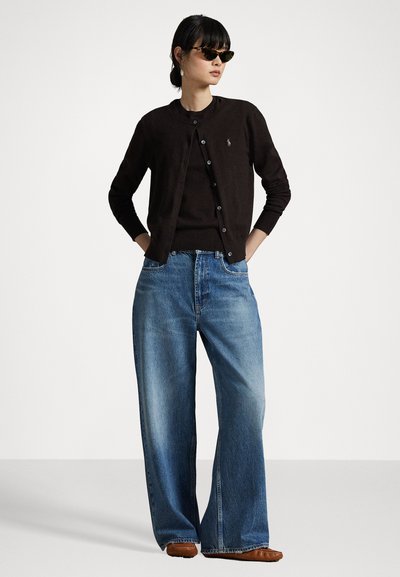 Čierny kardigán cez čierny top, doplnený svetlomodrými širokými džínsami. Hnedé topánky a slnečné okuliare dopĺňajú outfit.