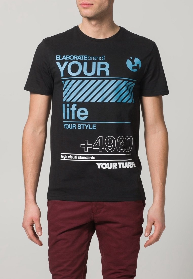 T-shirt en coton noir avec un motif graphique bleu, comprenant des rayures et des slogans. Porté avec un pantalon bordeaux. Manches courtes et col rond.