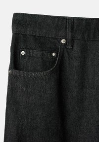 Czarne jeansy z denimu mają teksturowaną tkaninę, widoczne przeszycia, przednią kieszeń oraz metalowe guziki przy talii i otwarciu kieszeni.