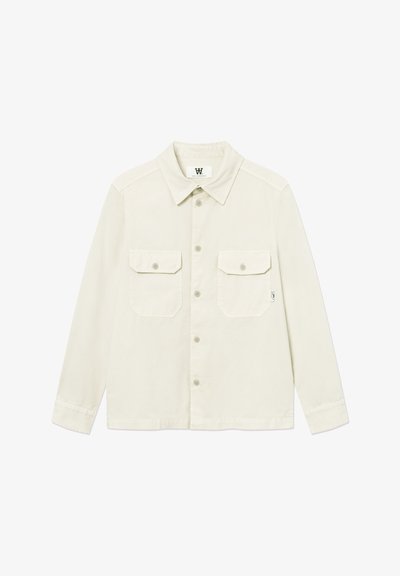 Chemise à manches longues de couleur blanc cassé avec boutons, deux poches à rabat sur le devant et un col classique, posée à plat sur un fond blanc.