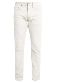 Jasnobeżowe spodnie sztruksowe o wąskim kroju, z przednimi kieszeniami, zamkiem błyskawicznym oraz metalowymi guzikami. Widoczna faktura tkaniny.