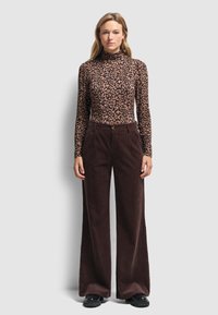 Zwierzęcy wzór w kolorze lamparta na golfie, dopasowany krój, połączony z brązowymi spodniami z okrycia w szerszym kroju. Czarne masywne obuwie dopełnia całość.