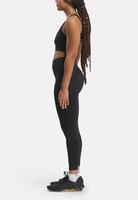 Top crop atletico nero e leggings high-waisted in tessuto liscio. Il modello indossa scarpe da ginnastica nere con suola in gomma color caramello e calzini bianchi alla caviglia.
