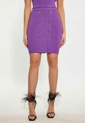 Fustă mini purpurie cu dungi, cu talie înaltă și design cu nasturi dubli, având butoane argintii strălucitoare. Tocuri negre cu bretele, accentuate cu pene.