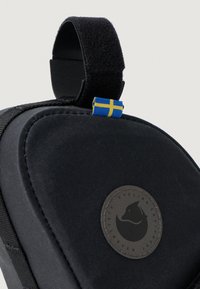 Melnas velosipēdu somas ar noapaļotu formu, teksturētu audumu, Velcro jostu un apļveida logo uzlīmi ar melnu dizainu un Zviedrijas karoga akcentu.