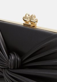 Clutch in pelle nera con una finitura texturizzata, caratterizzato da un design annodato e dettagli della chiusura a forma di cuore in tonalità oro.