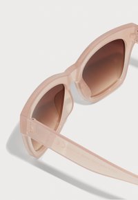 Ochelari de soare supradimensionați cu o ramă transparentă roz, lentile maronii cu degradé și un design elegant. Prezintă logo-ul pe tâmplă.