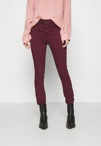 Burgundowe skinny jeans z wysokim stanem, wykonane z teksturowanej tkaniny. Połączone z luźnym różowym swetrem dzianinowym i czarnymi botkami za kostkę.