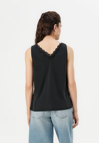 Top nero senza maniche con scollatura a V bordata in pizzo, caratterizzato da una vestibilità comoda e abbinato a jeans in denim chiaro.