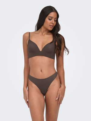 Woman with long dark hair wearing matching brown bra and high-cut underwear, posing against plain light background.