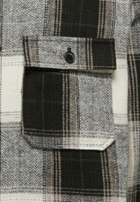 Wool flanelasta srajca z zelenim, belim in rjavim karirastim vzorcem, z žepom na prsih in črnim gumbom.