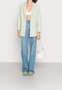 Světlezelený oversize blejzr, bílý crop top, modré džíny s vysokým pasem, zelené tkané sandály a malá bílá kabelka.