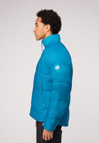 Veste d'hiver bleu sarcelle avec un col haut, des poches zippées et un accent logo sur la manche. Design texturé et matelassé avec une coupe ajustée.