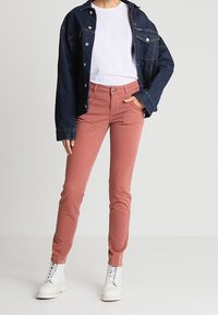 Tmavě modrá džínsová bunda, bílý tričko a růžové slim-fit kalhoty se jemnou strukturou, kombinované s bílými kotníkovými botami. Hlavní vizuální prvky zvýrazněny.