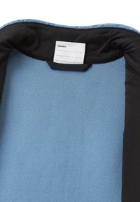 Blauer Stoff mit glatter Textur, schwarzen Akzenten und einem Etikett mit der Aufschrift "Ich war hier." Der Ausschnitt hat eine abgerundete Form.