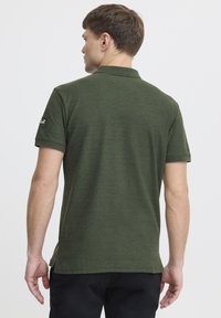 Grøn kortærmet polo t-shirt lavet af tekstureret stof, med en ribbet krave og et logo-patch på venstre ærme.