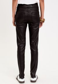 Pantalones de cuero sintético negros con un diseño ajustado, cinco bolsillos y una textura suave, combinados con zapatillas blancas y negras.