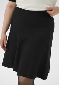 Falda negra hasta la rodilla hecha de una tela suave, con un diseño acampanado y una cintura elástica. Textura suave con líneas limpias.