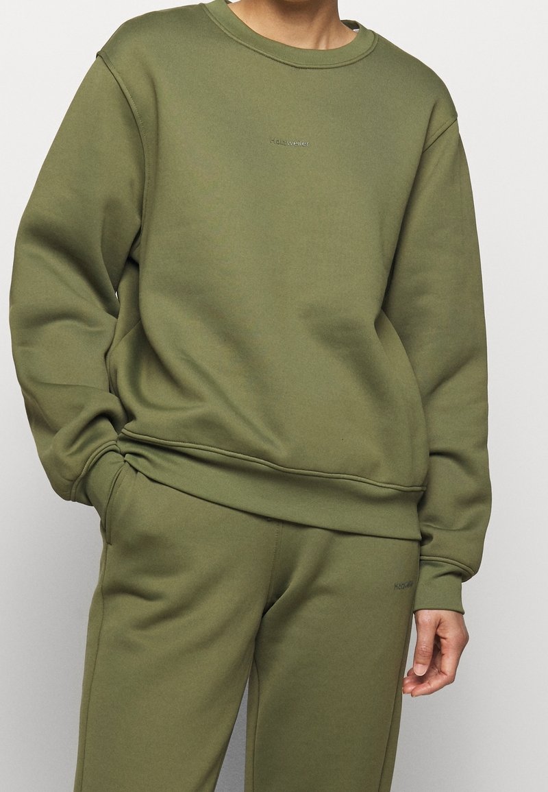 Olivgrön sweatshirt i avslappnad passform, med rund hals och ribbade muddar. Slät textur med diskret logotyp på bröstet.