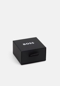 Scatola di cartone nera con superficie liscia e design a cassetto, dotata di maniglia in tessuto nero e della parola "BOSS" stampata in bianco sulla parte superiore.