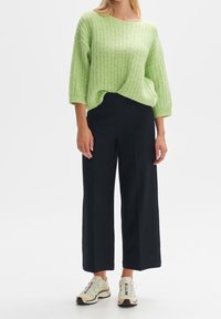 Pull tricot vert clair à coupe ample avec un motif texturé, associé à un pantalon large noir et des baskets beiges.