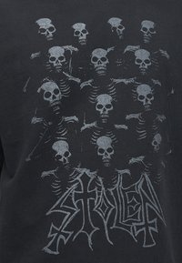 Πολλά γκρίζα κρανία και σκελετοί arranged πάνω από τη λέξη "STOLEN" σε στυλιζαρισμένη γοτθική γραμματοσειρά σε σκοτεινό υφασμάτινο φόντο.