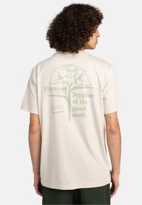 Camiseta de manga corta beige con diseño gráfico verde que presenta flores y texto en la parte posterior. Fabricada en suave material de algodón.