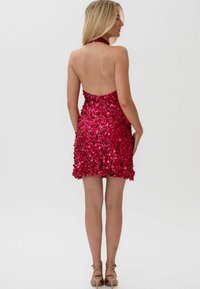 Halterska haljina u živopisnoj ružičastoj boji s cjelovitim dizajnom od svjetlucavih šljokica. Kratka, uska silueta s otvorenim leđima i lepršavim rubom.