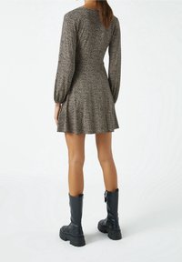 Dlouhý rukáv, přiléhavé šaty na béžovém podkladu s černým tečkovaným vzorem. Rozšířená sukně, měkká látka, kombinované s černými kotníkovými botami.