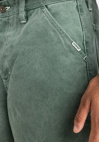 Green cotton shorts with a textured finish. Features a front pocket, brown button closure, and a small tag labeled "ELEMENT."