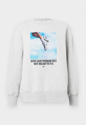 Sweat-shirt gris clair avec un graphisme d'une jambe chaussée de chaussures de sport, accompagné du texte : "QUI A DIT QUE LA FEMME N'ÉTAIT PAS FAITE POUR VOLER." Col rond.