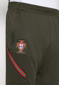 Mörkgröna träningsbyxor med en broderad Portugal-krehoa och en sidremsa i rött, grönt och svart. Har en strukturerad midja.