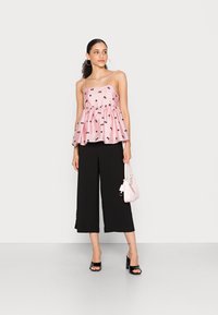 Top peplum rosa com padrões florais pretos, combinado com calças largas pretas. Acessorizado com uma pequena mala rosa e sapatos de salto pretos.