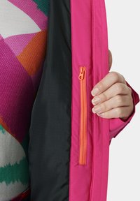 Roze jacksvoering met een contrasterende zwarte voering. Bevat een oranje ritszak aan de binnenzijde aan de linkerkant. Stevige textuur.