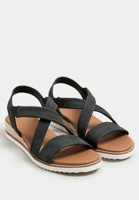 Mustat risti-strap sandalit, joissa on ruskea pohja, pehmeä pinta ja valkoinen ulkopohja. Sisältää espadrille-tyylisen korkean varren lisäämä än korkeutta.