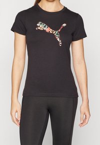 Camiseta negra con cuello redondo y mangas cortas que presenta un colorido logo floral de Puma. El material parece suave, con un diseño ajustado.