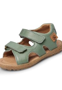Zielona skórzana sandały z zapięciem na rzep, otwartym wzorem, brązową wkładką i teksturowaną gumową podeszwą. Posiadają wycięcia jako ozdobne akcenty.