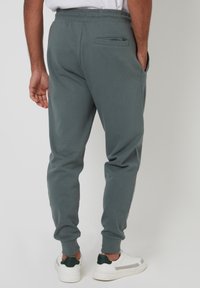 Grå joggingbukser med elastisk taljebånd, smal pasform, sidelommer og en baglomme, kombineret med hvide sneakers med grønne detaljer.