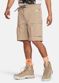 Beige cargoshorts med flera zipfickor, justerbar dragsko i midjan, tekniskt tyg, matchat med beige vandringsskor och strumpor med orange-rand.
