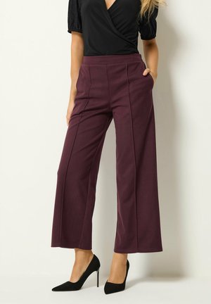 Mujer con pantalones burdeos de talle alto y pernera ancha con costuras delanteras, camiseta negra de manga corta y tacones altos negros puntiagudos.