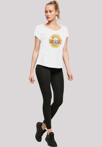 White cotton t-shirt with a circular graphic featuring a skull and roses, paired with black leggings and black athletic shoes.