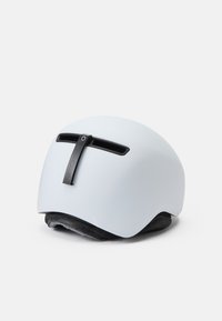 Hvid hjelm med mat finish, udstyret med sorte ventilationsslidsser og en frontalrem til justering. Blød grå indvendig polstring synlig.